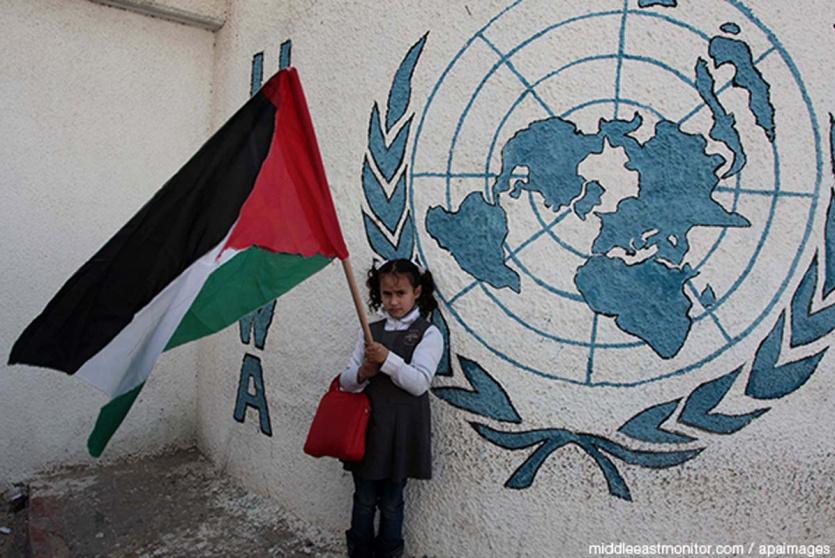 طفلة تحمل العلم الفلسطيني أمام مقر للاونروا